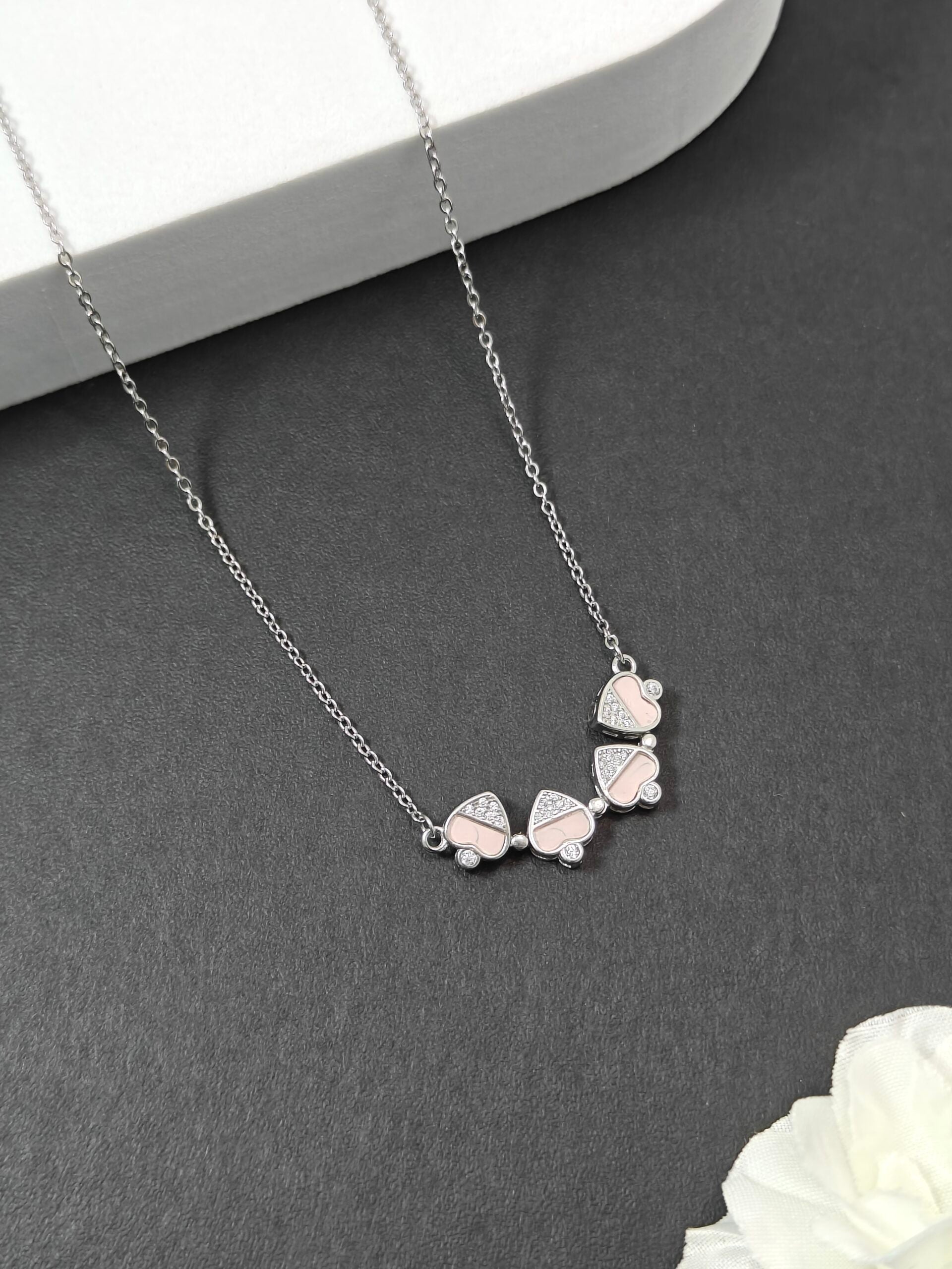 Silver necklace with leaf-shaped pendants on a gray surface with a white flower.